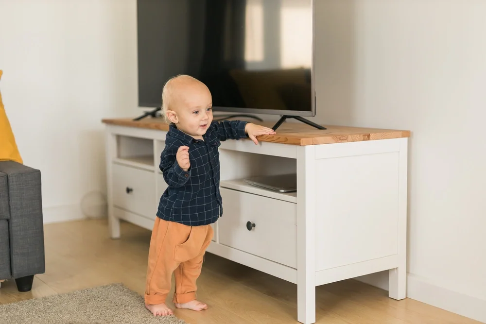 Toddler holding on to a tv stand